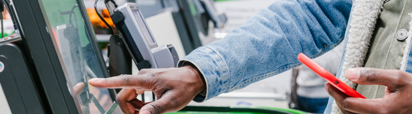 The finger of an African man in close-up at the supermarket checkout selects the desired product on the electronic screen of the cash register with a phone in his hands